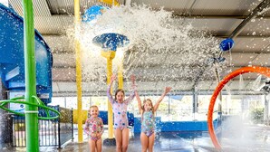 Un área de juegos acuáticos con múltiples chorros de agua y una estructura verde.