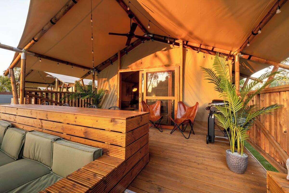 An outdoor seating area with wooden furniture and a covered section with a ceiling fan.
