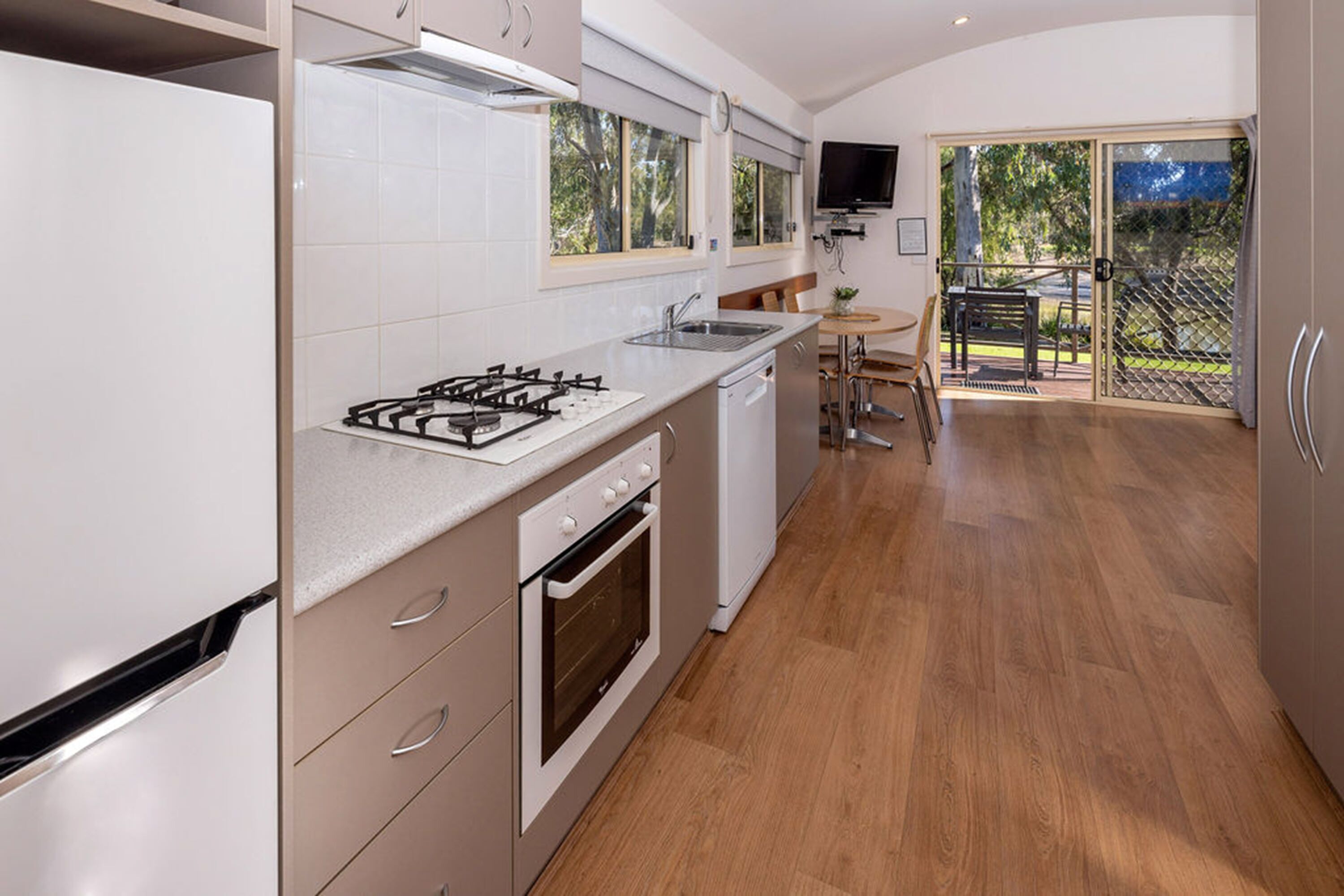 A modern kitchen with a gas stove, oven, and dishwasher, a dining area with a table and chairs, and a sliding glass door leading to an outdoor area.