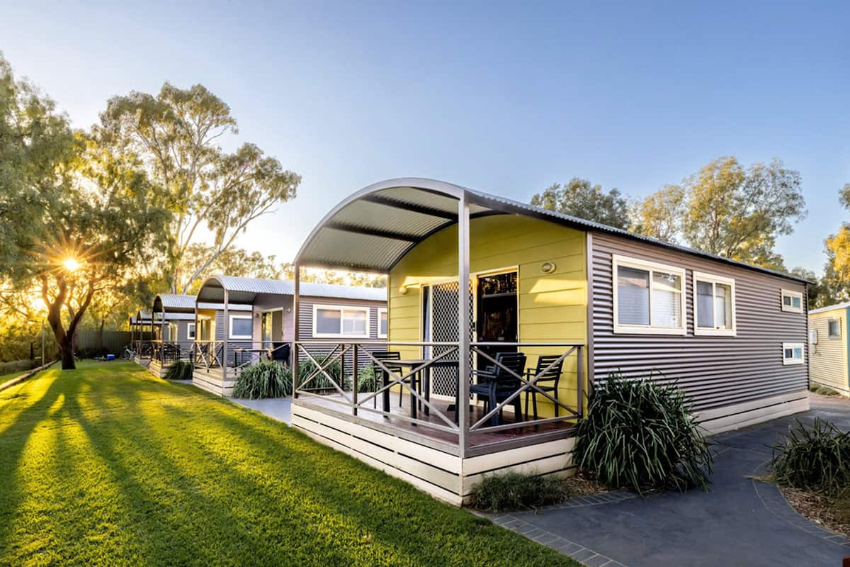 A mobile home with a covered porch, a small deck, and a well-maintained lawn.