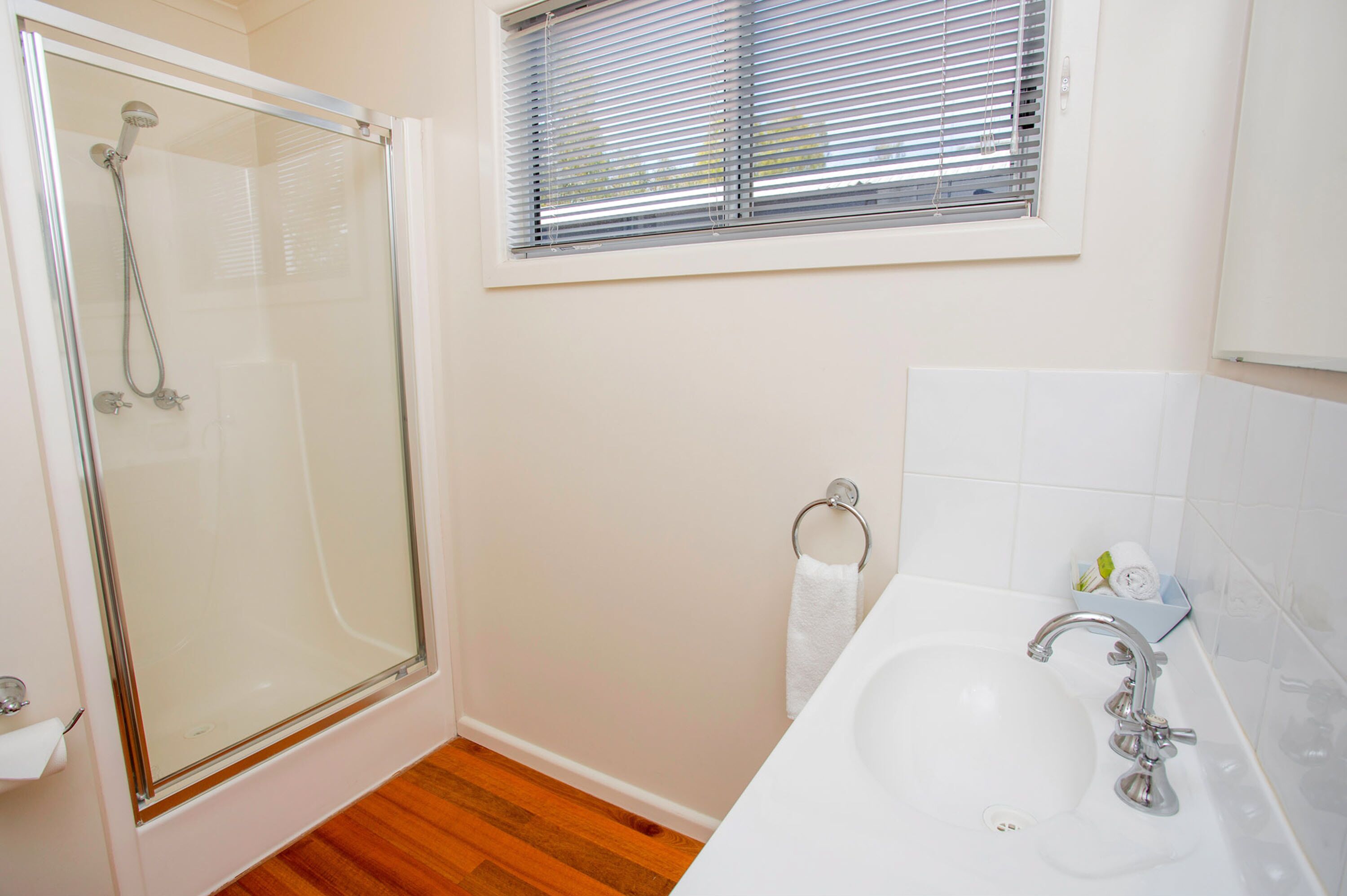 A bathroom with a glass-enclosed shower, a white sink, and a window with blinds.