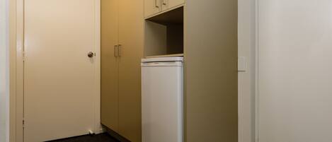A room with a white door, beige walls, a white refrigerator, and a carpeted floor.