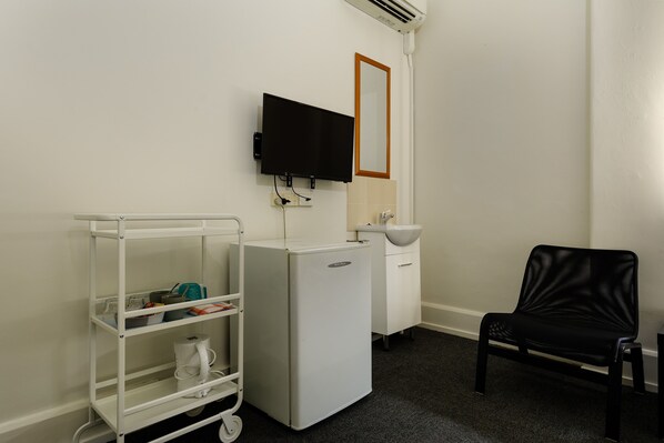 A small, clean room with a white refrigerator, a sink, a black chair, and a white shelf unit.