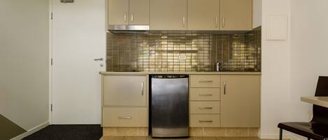 A compact kitchen with beige cabinets, a stainless steel dishwasher, and a tiled backsplash.