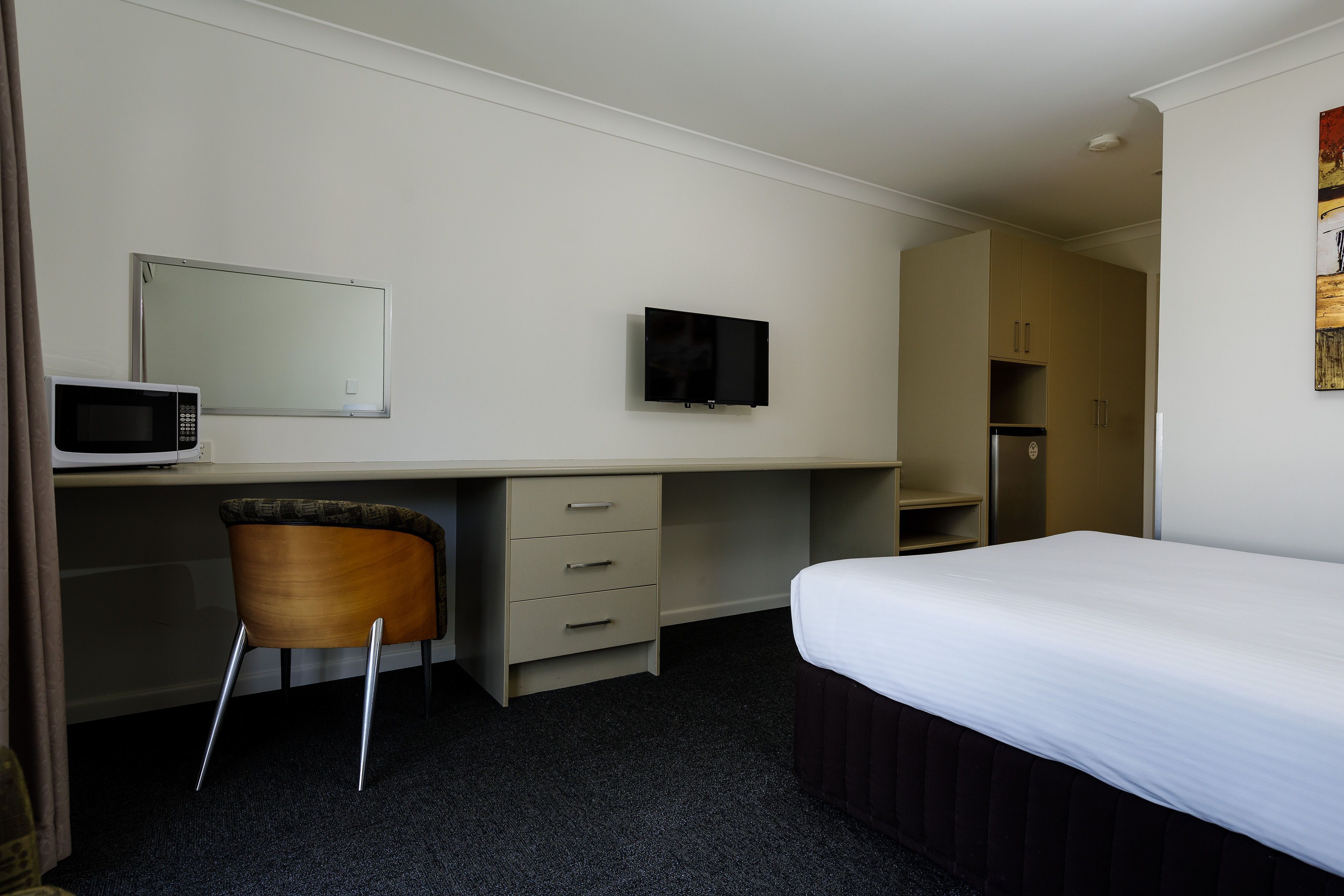 A hotel room with a bed, a desk with a chair, a television, a microwave, and a refrigerator.