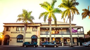 A two-story building with the sign "Waterloo Bar Hotel". There are palm trees in front, and cars parked on the street.