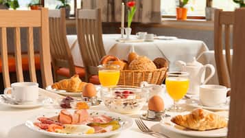 Ein Frühstückstisch mit Croissants, Eiern, Schinken und Obst auf Tellern, dazu Orangensaft und Kaffee.