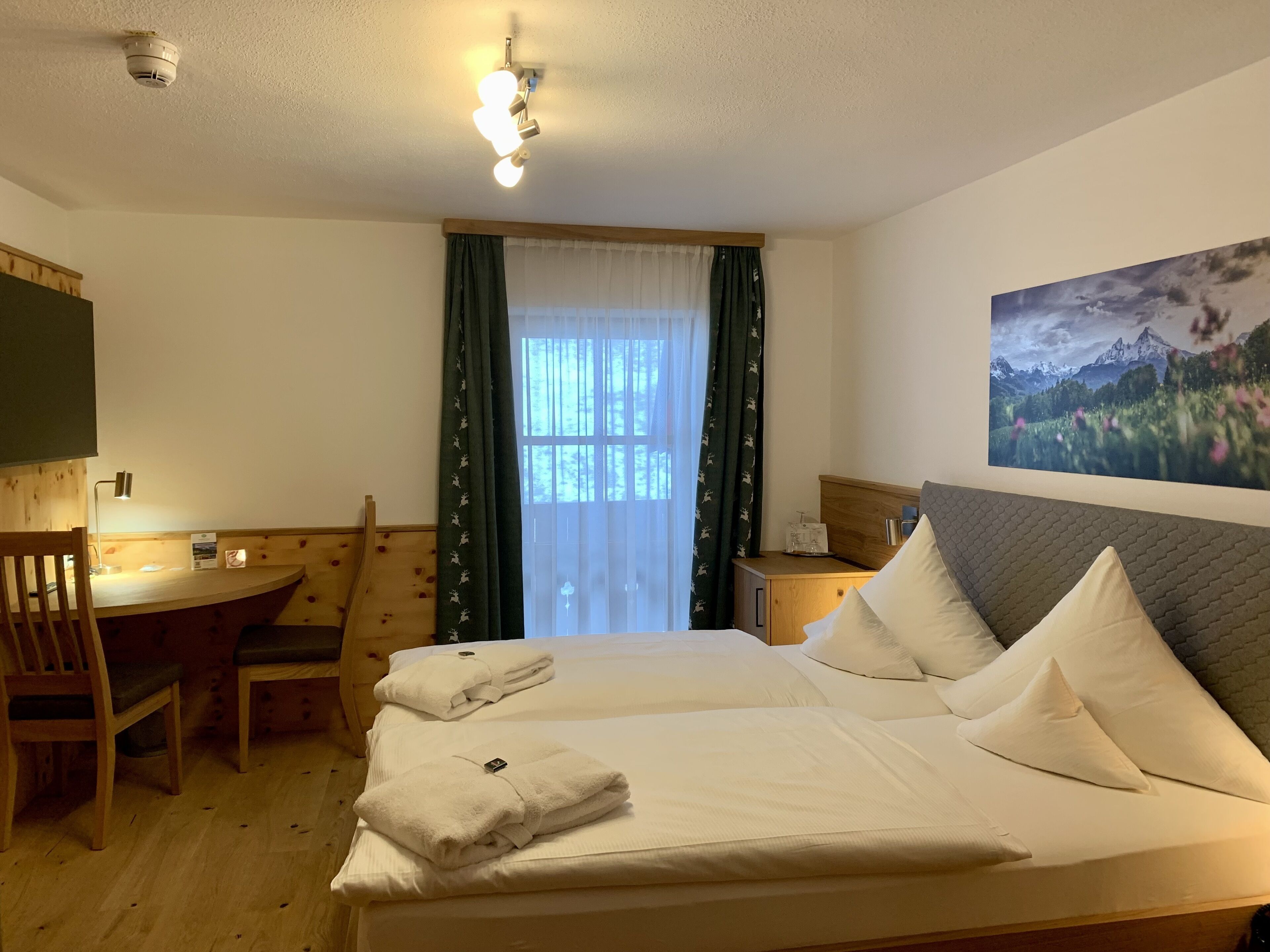 Une chambre d’hôtel avec un lit, un bureau, une chaise, une table de chevet et un tableau au mur.