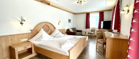 Ein Hotelzimmer mit einem hölzernen Bett, einem Schreibtisch, einem Sessel, einem Fernseher und einem roten Vorhang mit Rentier-Muster.