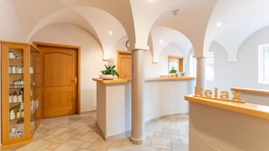 A hotel lobby with a wooden reception desk, a glass display case with toiletries, and a large pillar. - Naturhotel Reissenlehen (Bischofswiesen)
