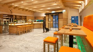 A modern interior with wooden beams, a bar area, seating, and a kitchen. - Naturhotel Reissenlehen (Bischofswiesen)