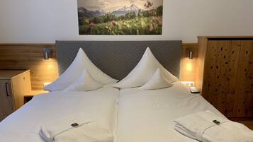 A double bed with white linens and pillows, a wooden headboard, and a painting of a mountain landscape above.