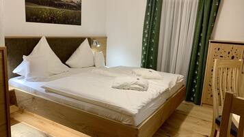 A neatly made bed with white linens and pillows, a wooden headboard, a wall-mounted lamp, and a painting of a landscape.