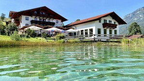 A hotel with a clear view of the lake, outdoor seating, and mountain backdrop. - Naturhotel Reissenlehen (Bischofswiesen)