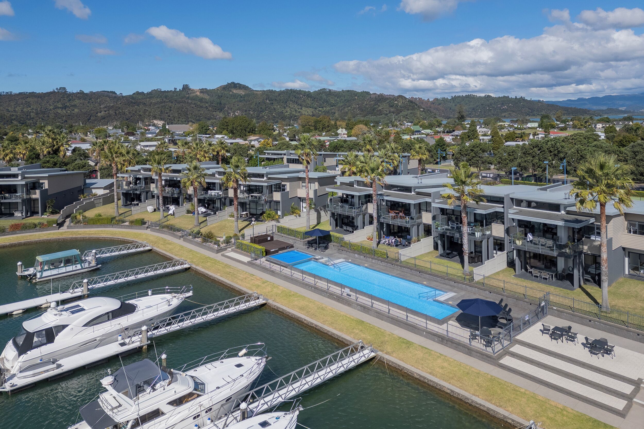 A marina with several yachts docked, a swimming pool, and modern buildings with balconies.