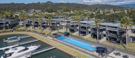 A marina with several yachts docked, a swimming pool, and modern buildings with balconies.