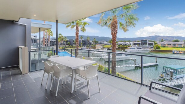 A balcony with a white table and chairs, overlooking a marina with boats and palm trees.