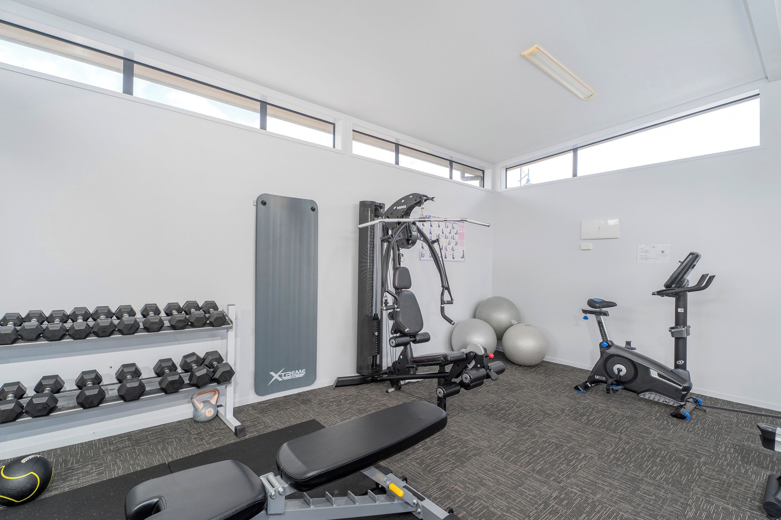 A gym with dumbbells, a weight bench, an elliptical, and exercise balls.