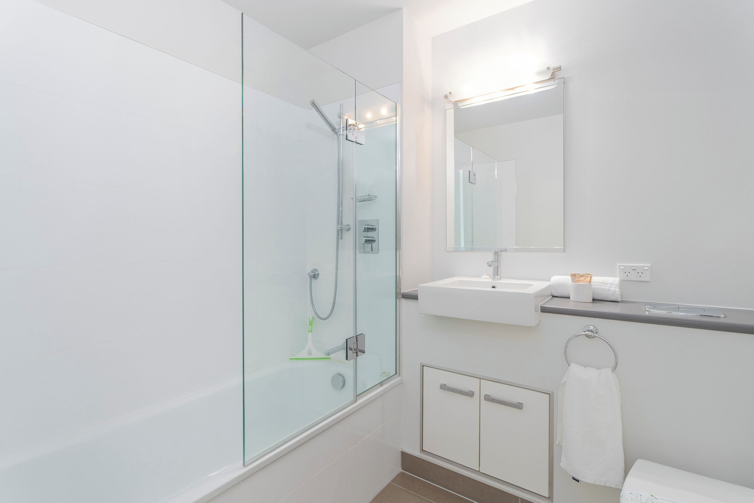 Un baño moderno con cabina de ducha de vidrio, lavamanos blanco y espejo sobre él.