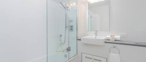 Un baño moderno con cabina de ducha de vidrio, lavamanos blanco y espejo sobre él.