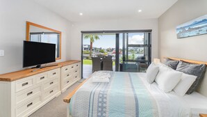 A bedroom with a large bed, a TV on a wooden dresser, and a balcony with a view.