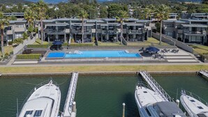 A marina with boats docked, a swimming pool, and modern buildings with balconies.