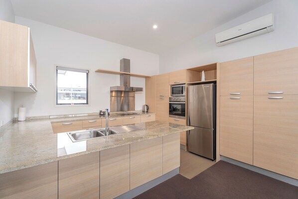 Una cocina moderna con un refrigerador de acero inoxidable, microondas y estufa, armarios de madera y un ventanal con vista a la ciudad.