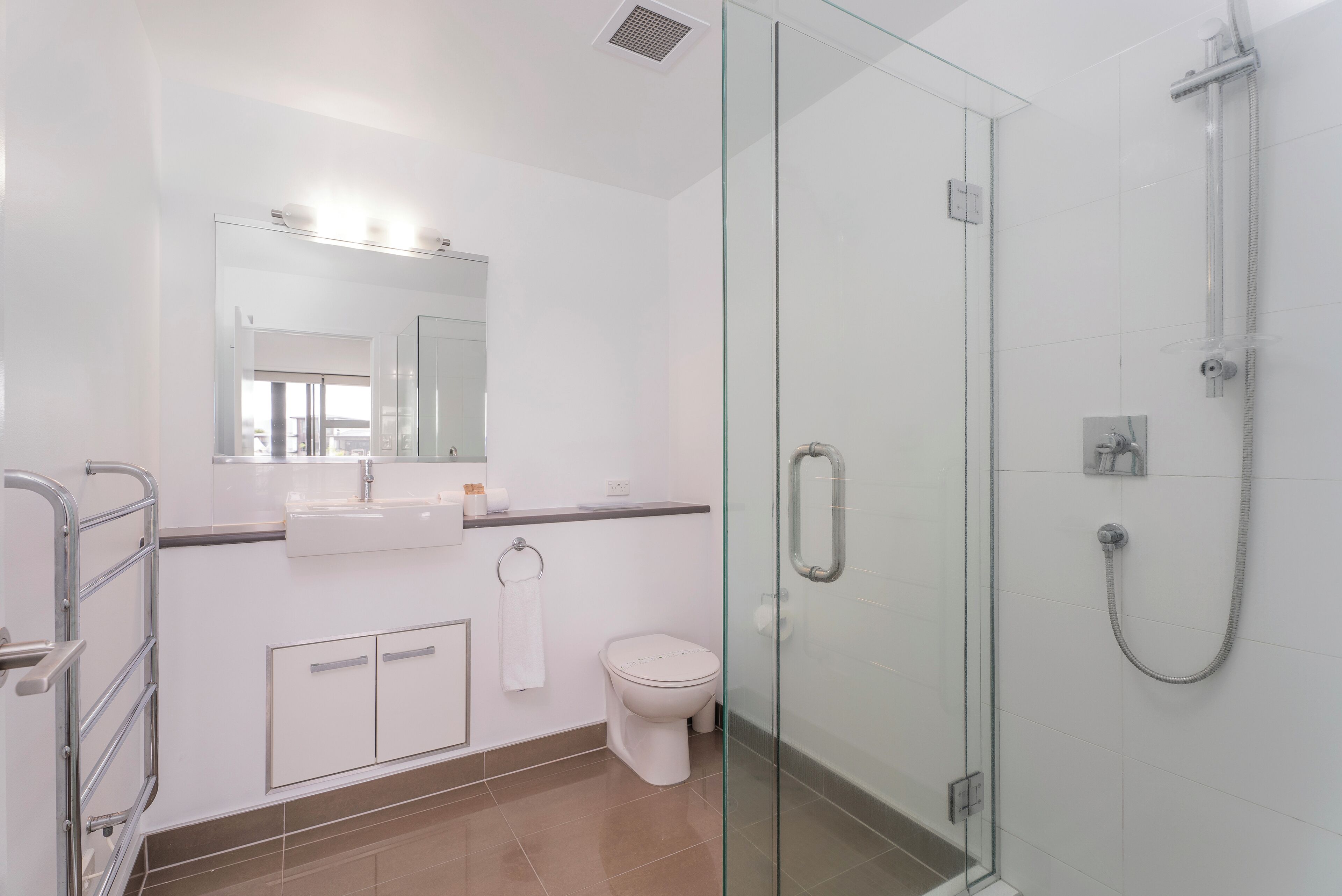 A modern bathroom with a glass shower enclosure, a white toilet, and a sink with a mirror above it.