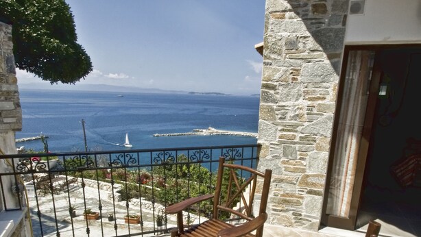 A wooden table and chairs on a balcony with a stone wall and a view of the sea. - Aegean Wave Hotel (Skopelos)