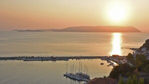 A marina with boats docked, a pier extending into calm waters, and a backdrop of hills during sunset. - Aegean Wave Hotel (Skopelos)