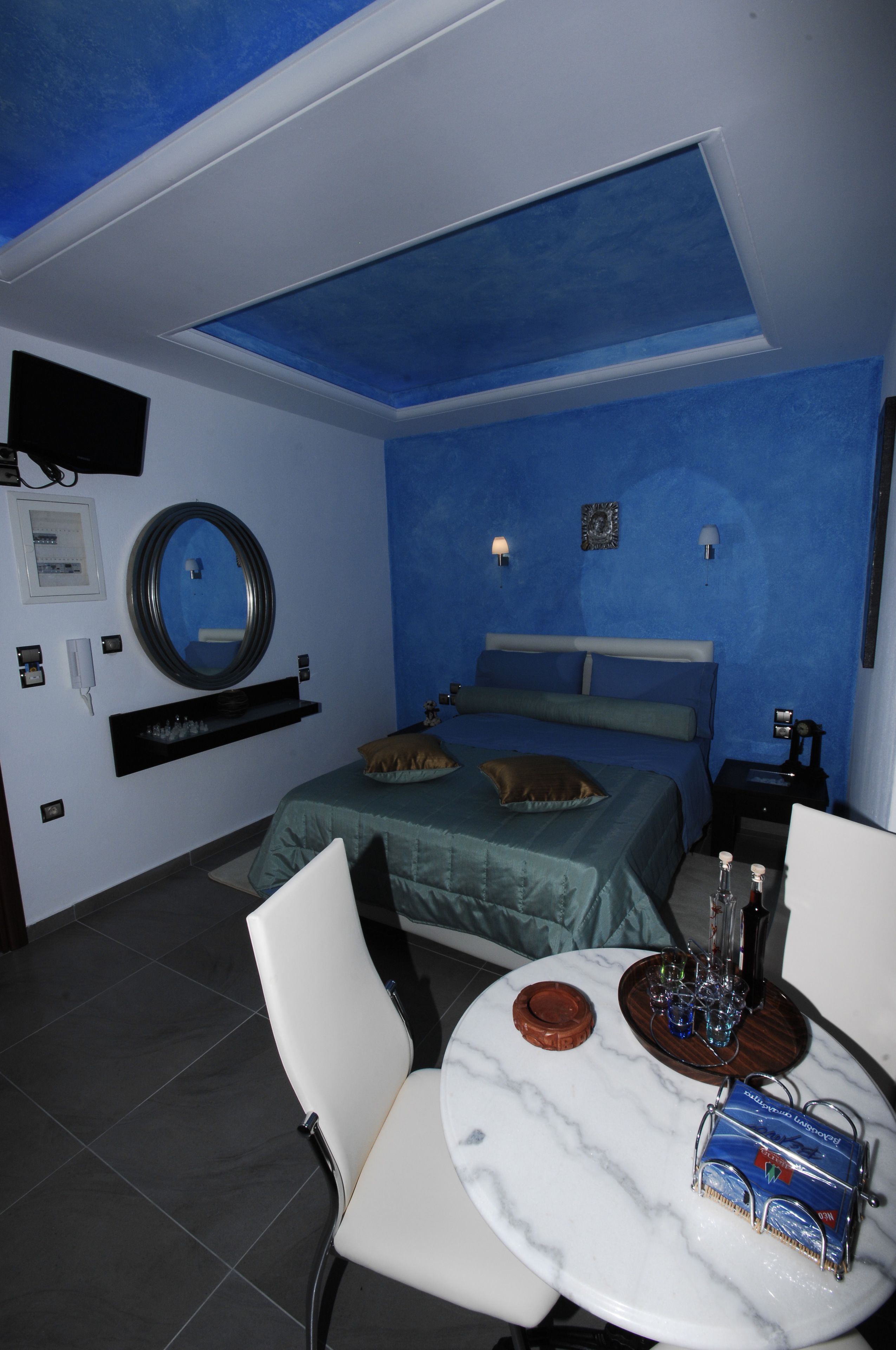 A bedroom with a bed, bedside tables, a round mirror, a TV, and a small dining table with chairs.