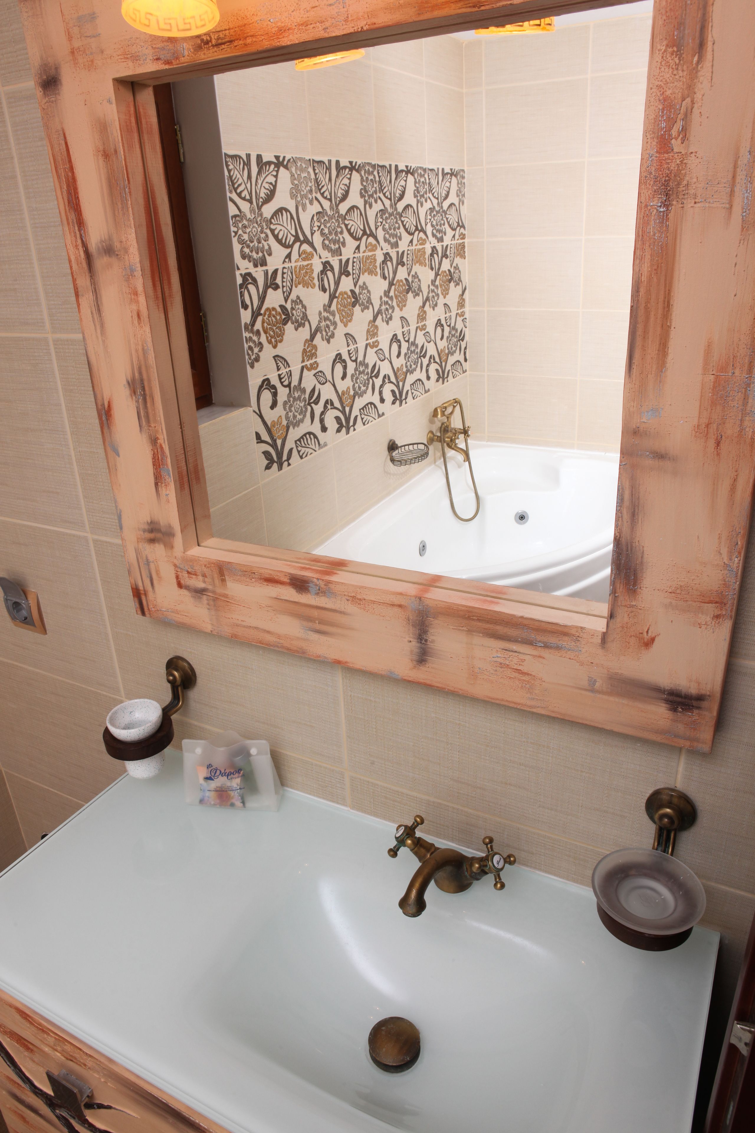 A bathroom with a white sink, a mirror with a distressed frame, and a patterned shower wall.