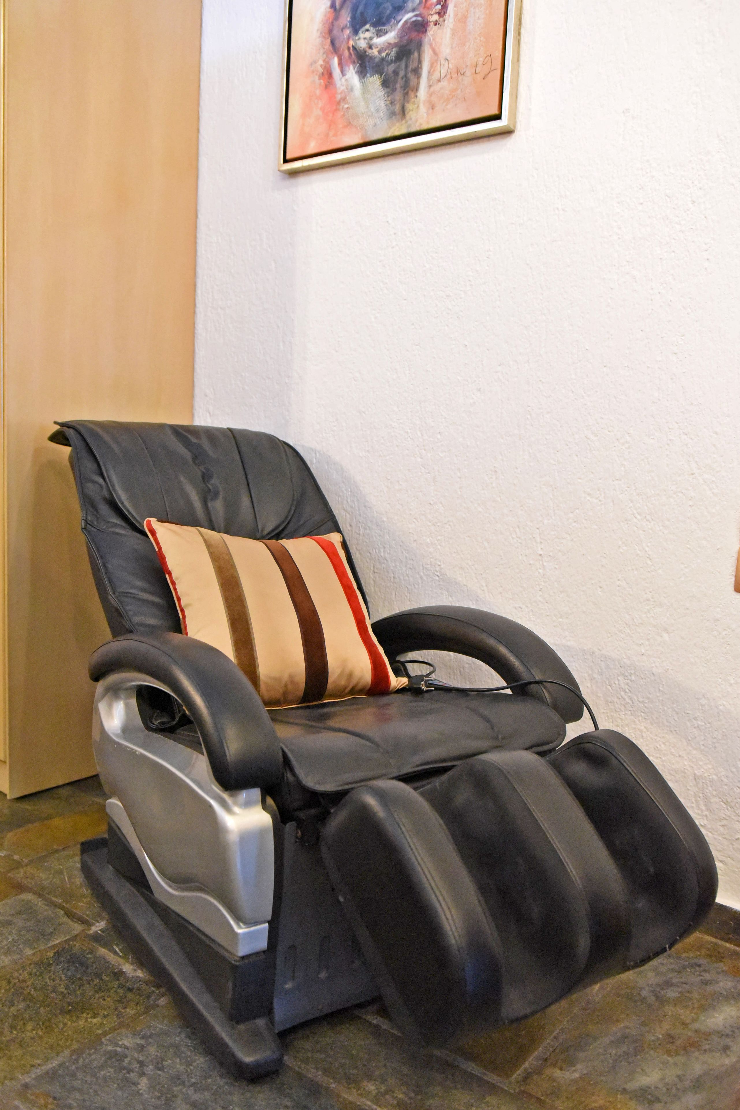 A massage chair with a striped pillow, positioned against a wall with a framed artwork above it.