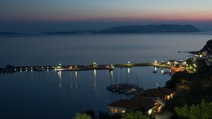 A coastal marina at dusk with boats docked, a pier extending into the water, and buildings along the shore. - Aegean Wave Hotel (Skopelos)