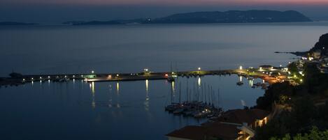 Un puerto costero al atardecer con barcos amarrados, un muelle que se adentra en el agua y edificios a lo largo de la costa.