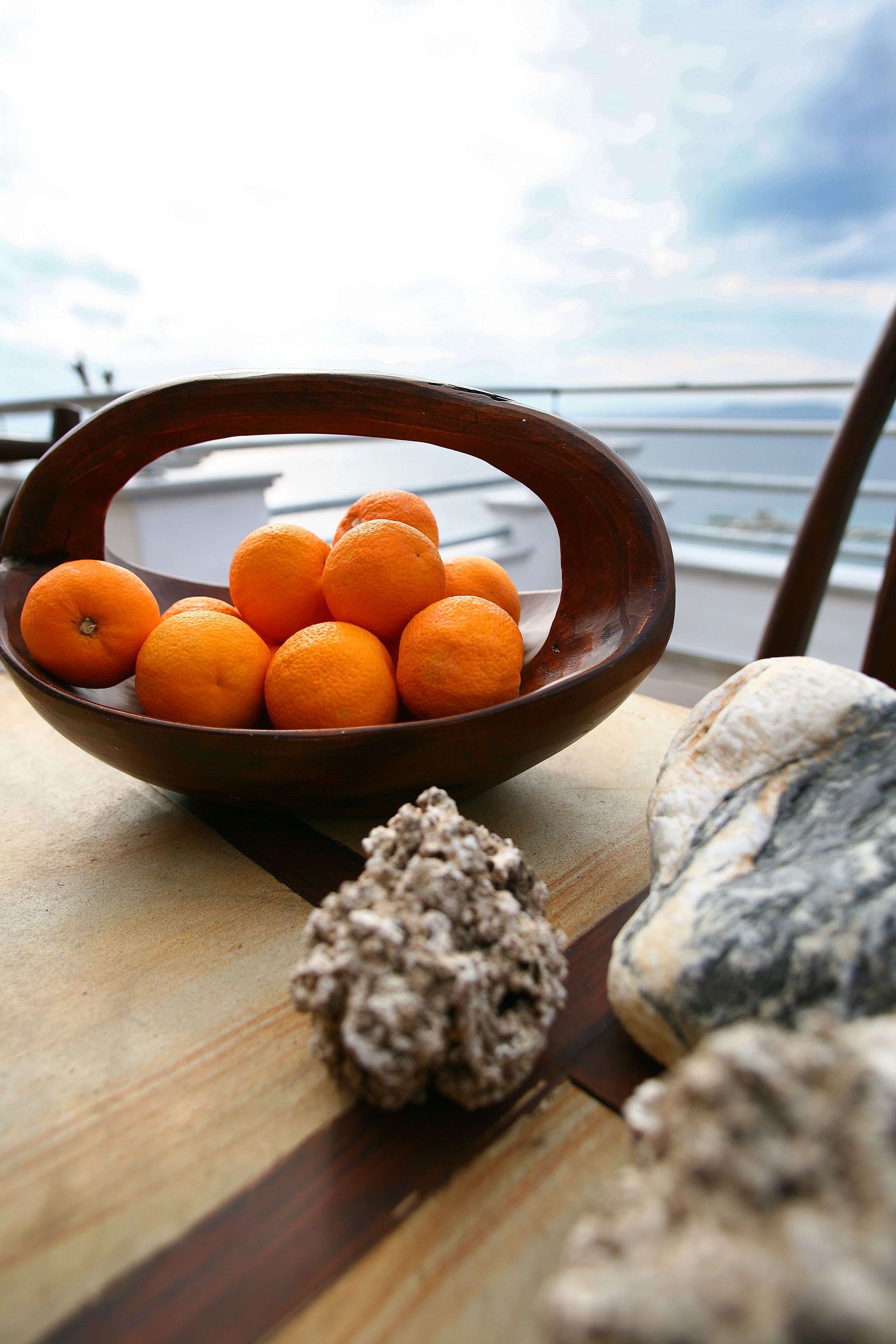 Un saladier en bois rempli d’oranges, posé sur une table, avec la mer en toile de fond.
