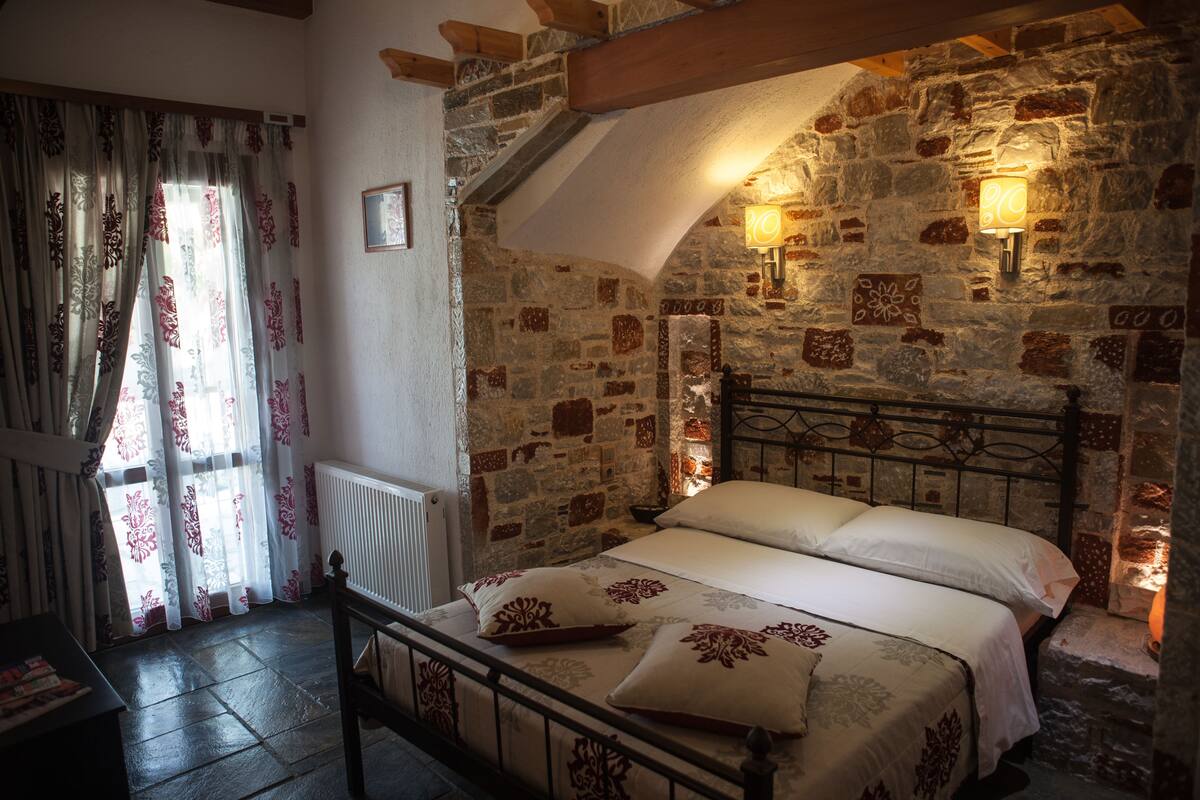 A bedroom with a stone wall, a bed with white linens, and a wooden headboard.