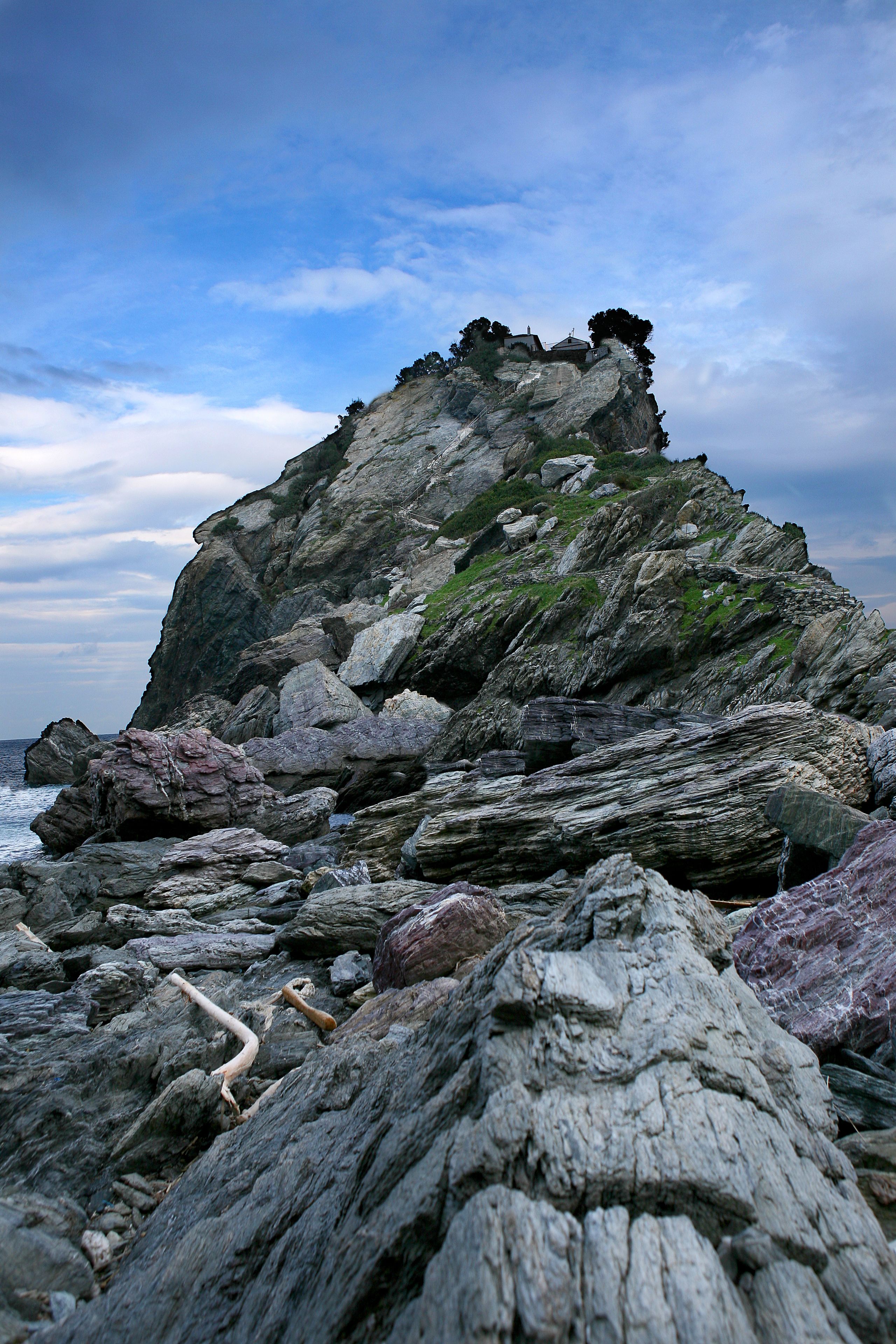 A rocky coastal landscape with a prominent rock formation and a small building on top.
