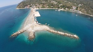 An aerial view of a coastal area with a rocky breakwater, clear turquoise waters, and a hillside with buildings. - Aegean Wave Hotel (Skopelos)