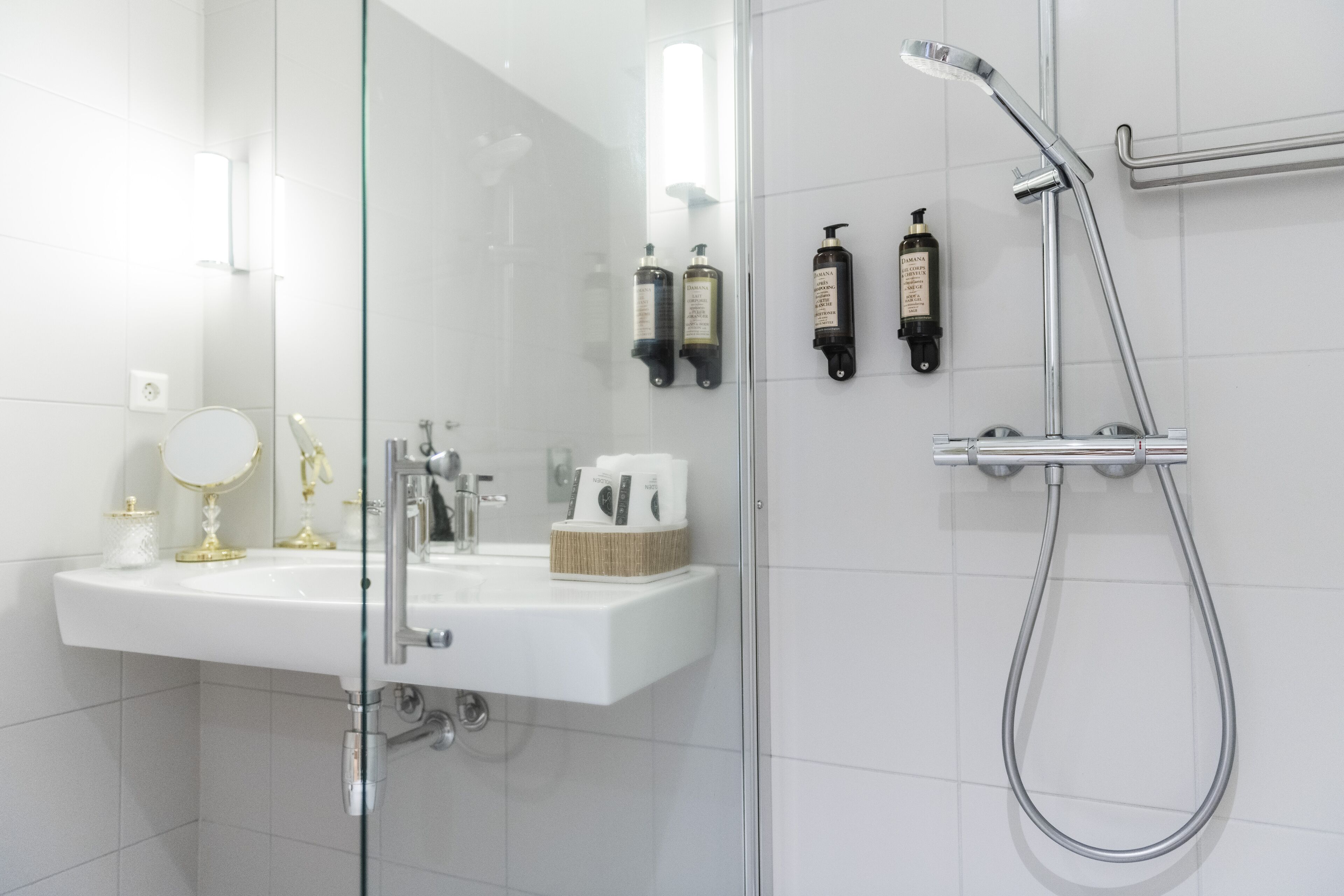 Une salle de bain moderne avec une douche à parois de verre, un lavabo blanc et deux étagères murales pour les articles de toilette.