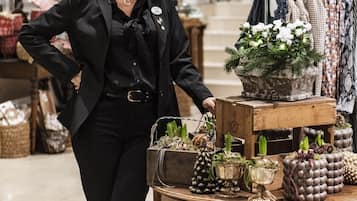 A woman standing next to a display table with various items including potted plants and clothing.