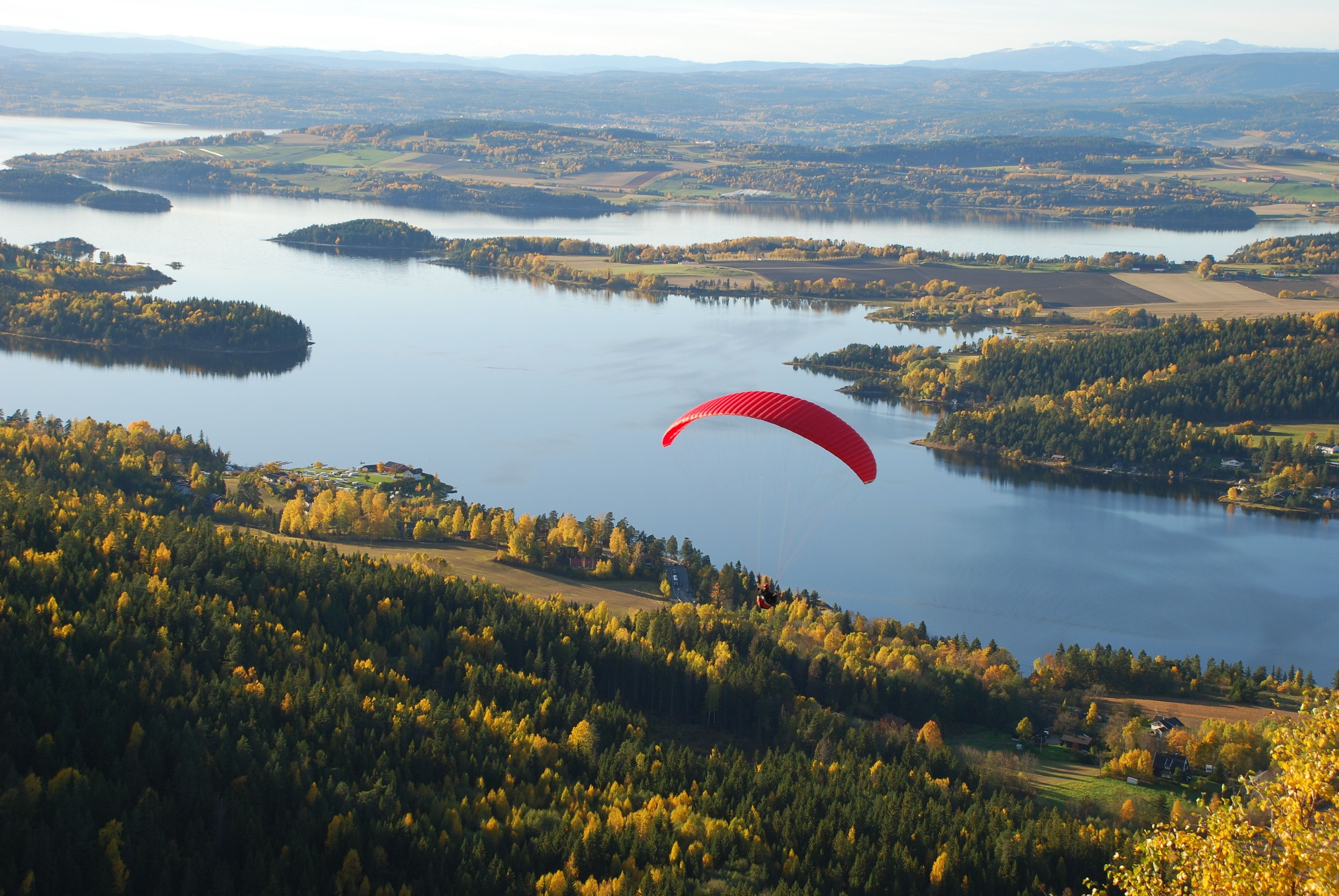 A person paragliding over a lake surrounded by forested hills.