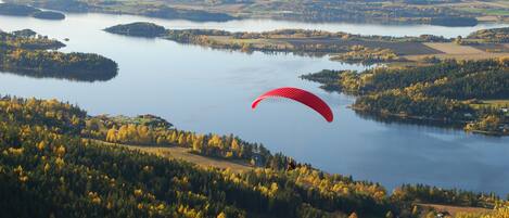 Une personne pratiquant le parapente au-dessus d’un lac, entouré de collines boisées.