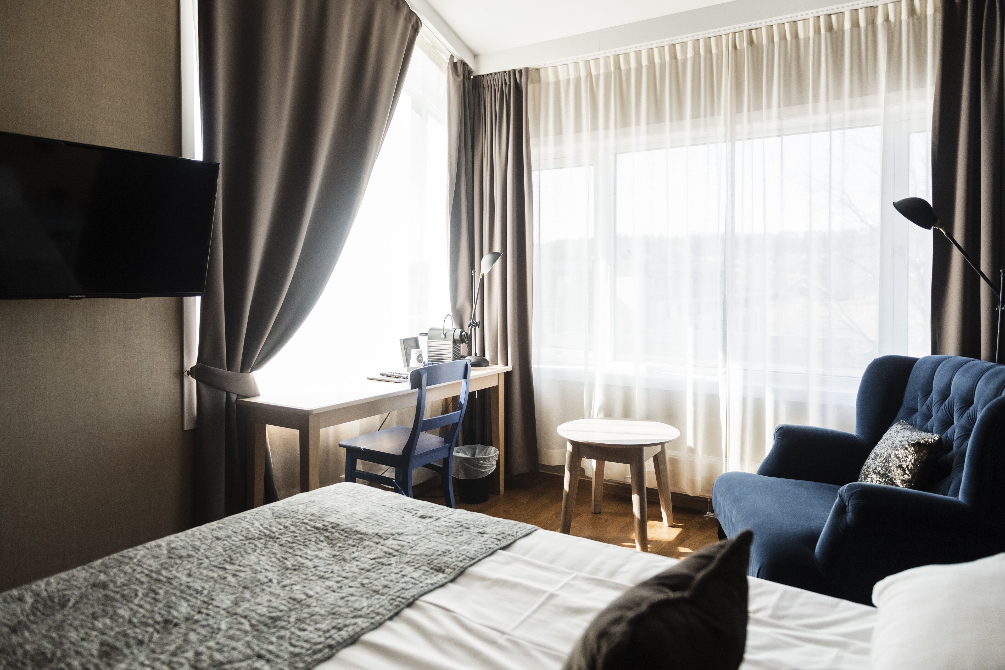Habitación de hotel con cama, escritorio, silla, mesita pequeña y televisor montado en la pared.