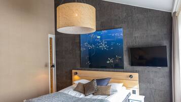 Une chambre moderne avec un grand lit, un téléviseur fixé au mur et une œuvre d’art murale originale.