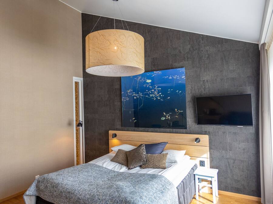 Une chambre moderne avec un grand lit, un téléviseur fixé au mur et une œuvre d’art murale originale.