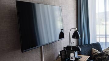 Una habitación de hotel moderna con un televisor de pantalla plana grande montado en la pared, un escritorio con una lámpara, una cafetera y un control remoto.