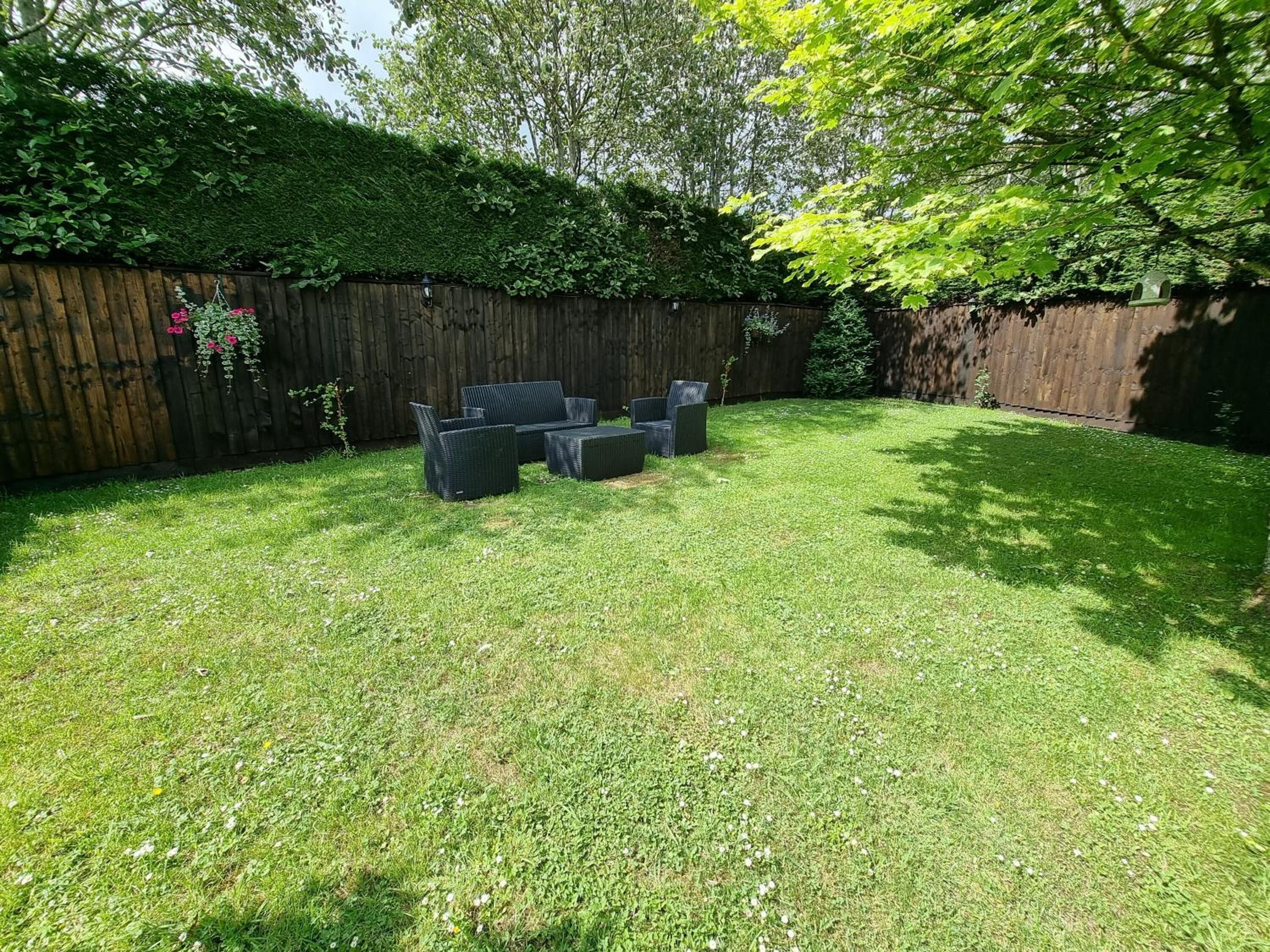 Un jardin avec une clôture en bois, une pelouse verdoyante et du mobilier d’extérieur.