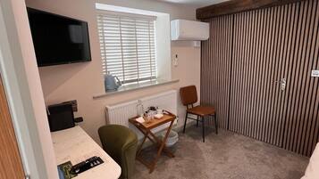 A compact room with a bed, a desk with a chair, a television, and a window with blinds.