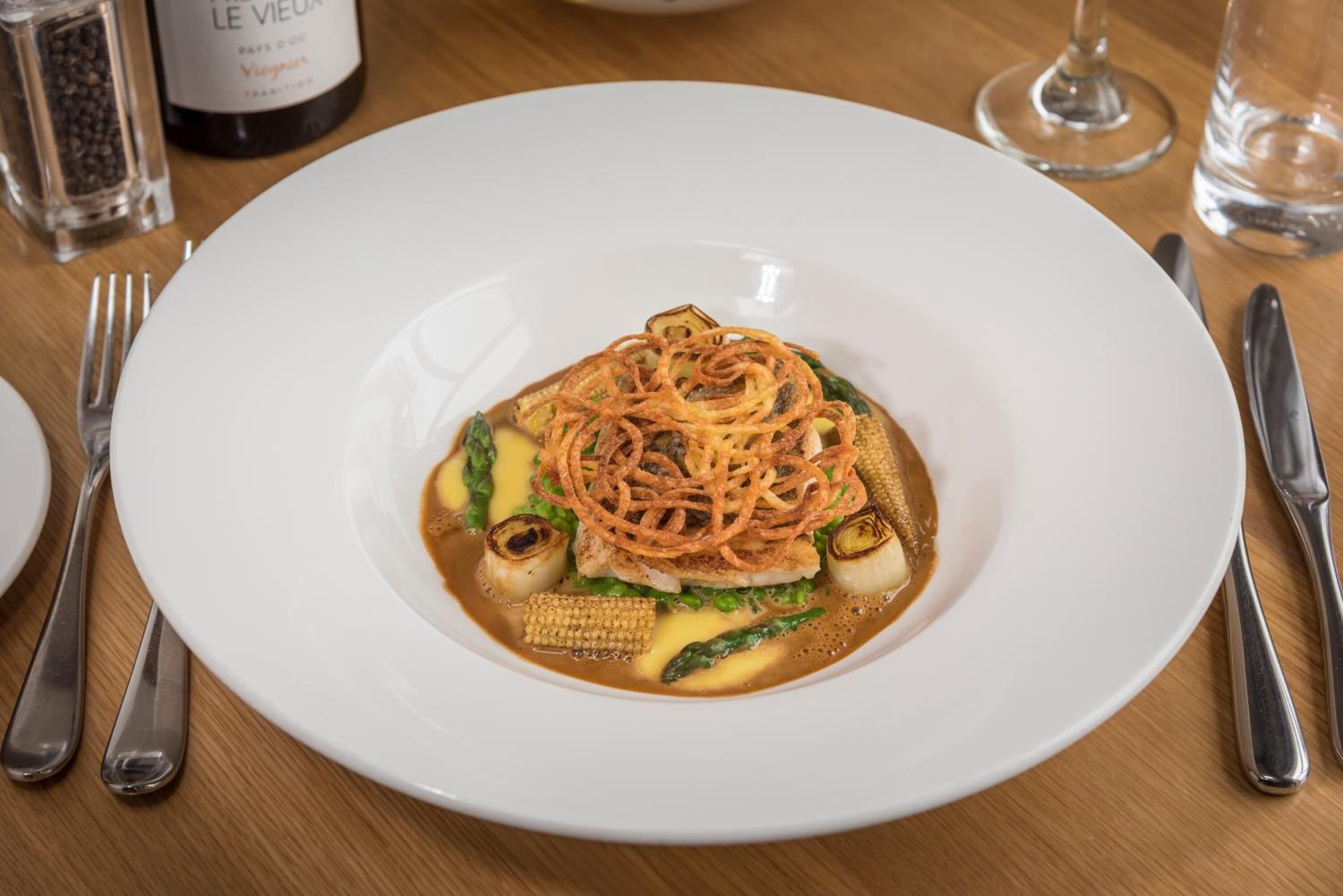 Un plato blanco con un guiso de fideos, verduras y salsa sobre una mesa de madera.